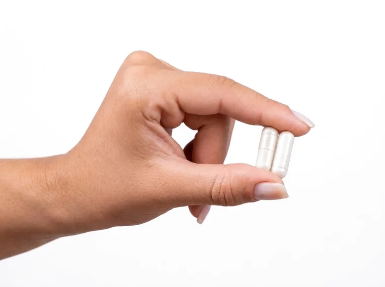 Mão segurando as duas cápsulas de Trimagnésio da dose diária